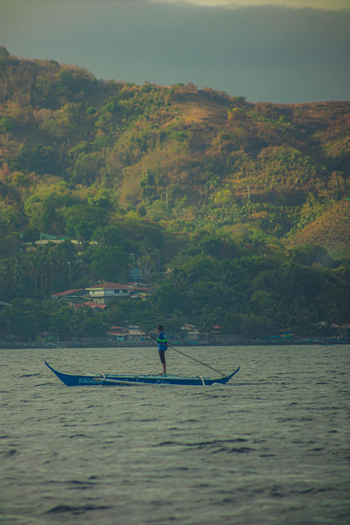 Man in traditional canoe enjoying a peaceful ride on a serene lake surrounded by lush hills.
